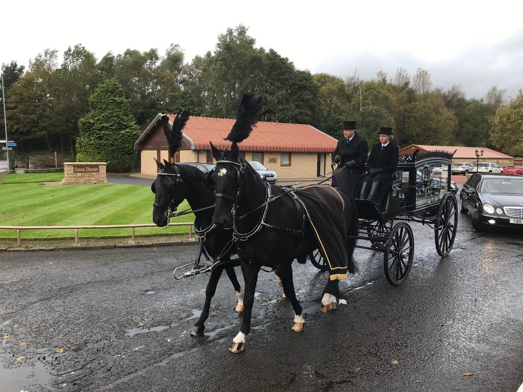 A horse drawn hearse outside of the JD Lawson funeral directors building